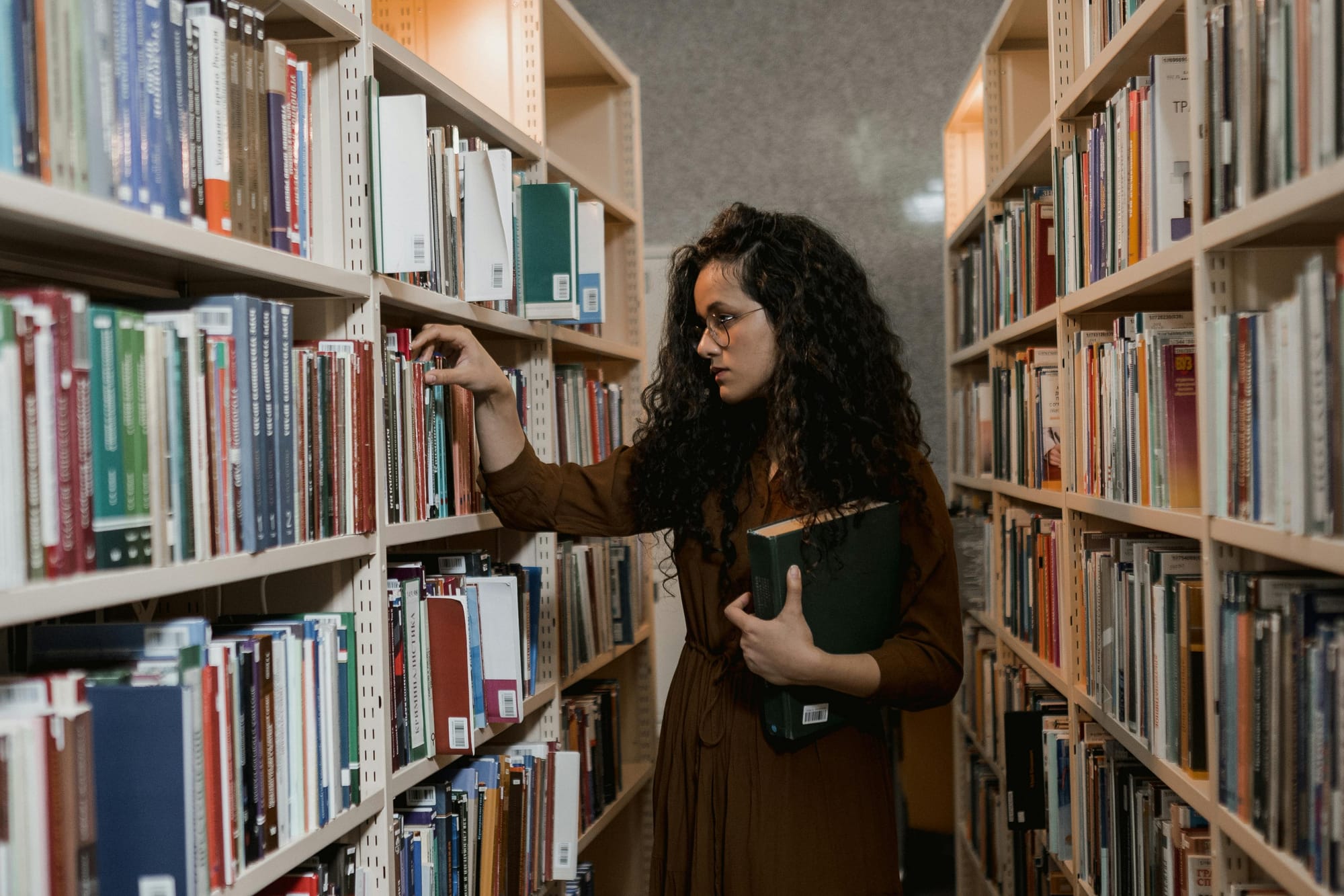 A woman in a library choosing a book from a shelf