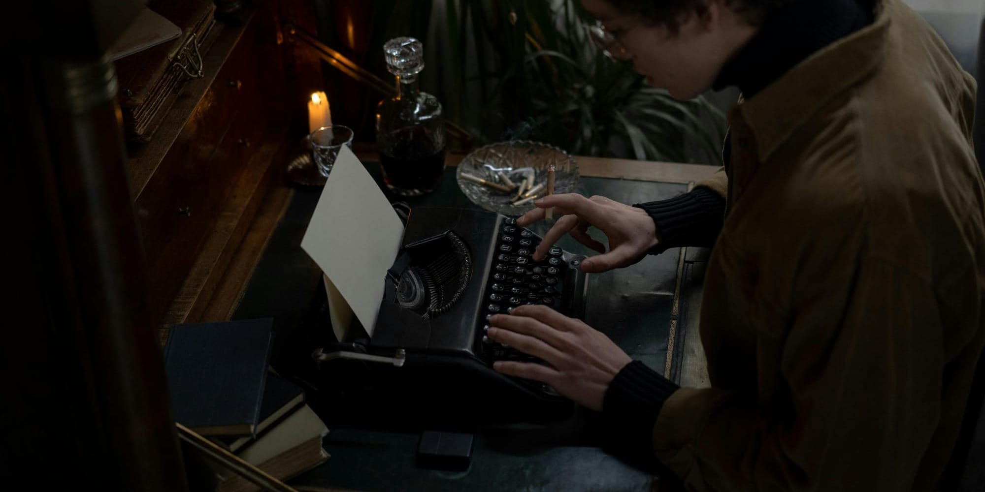 Person writing at vintage typewriter in a dimly lit room