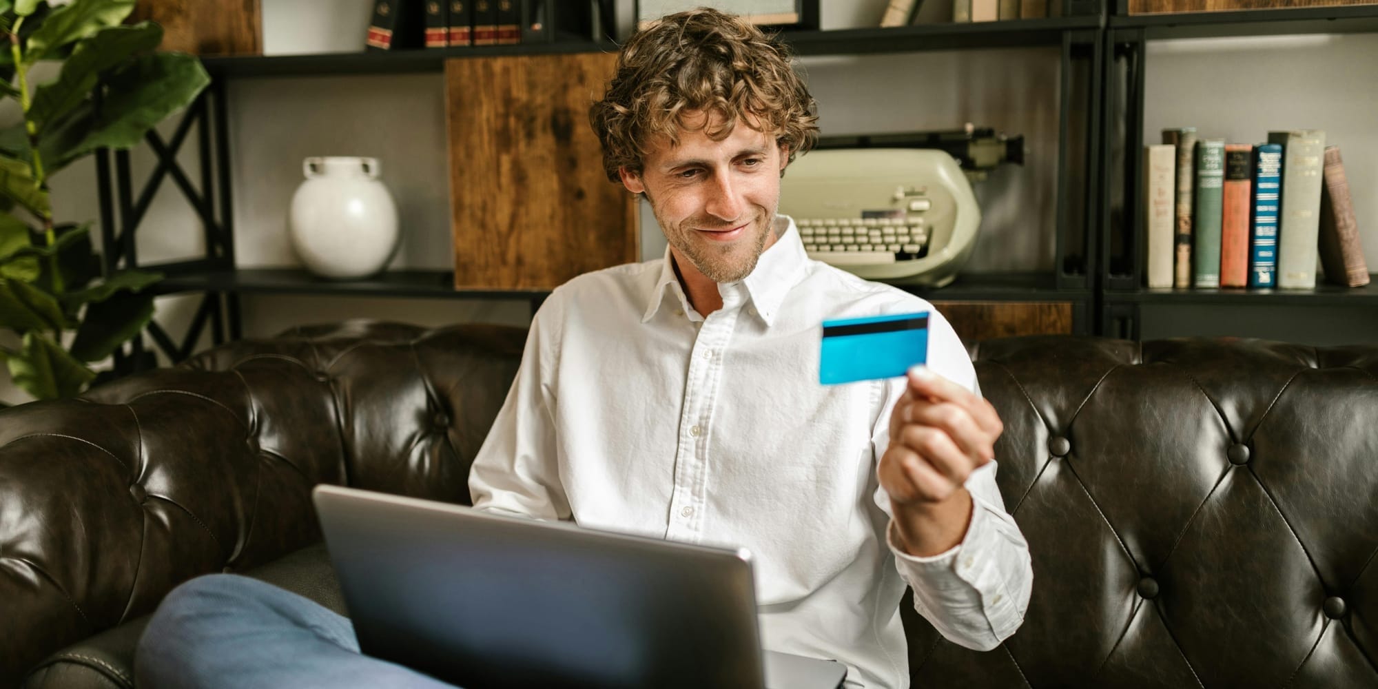 a man smiling at his credit card while sitting with a laptop