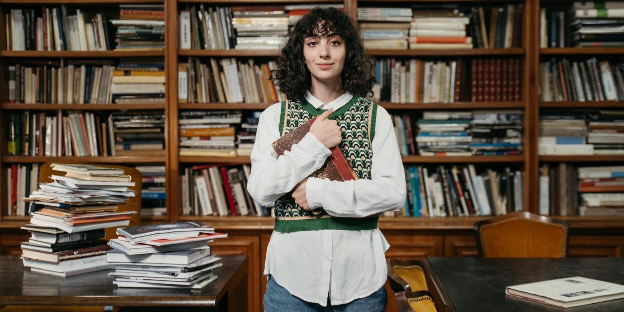 woman holding an old book close to her chest in a library full of books
