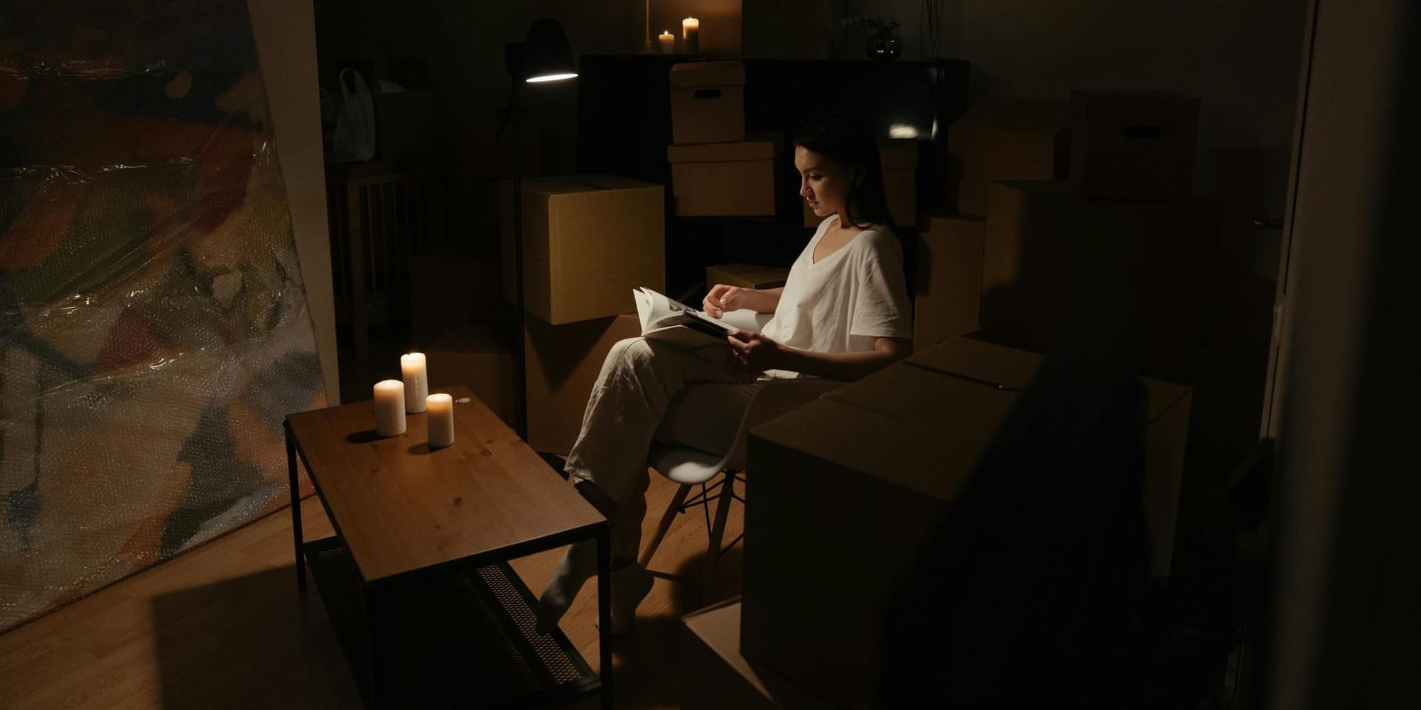 Woman reading a book alone by candlelight surrounded by moving boxes