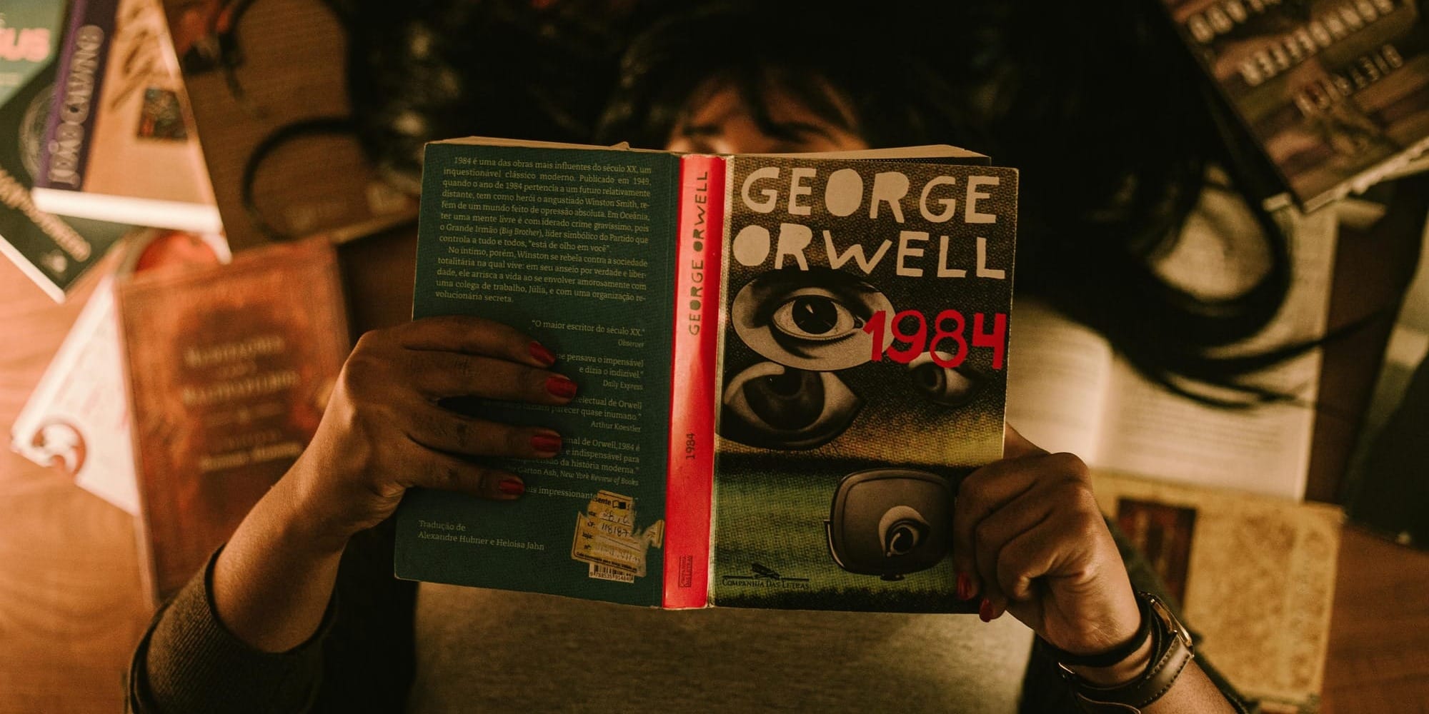 Person reading 1984 by George Orwell surrounded by other books