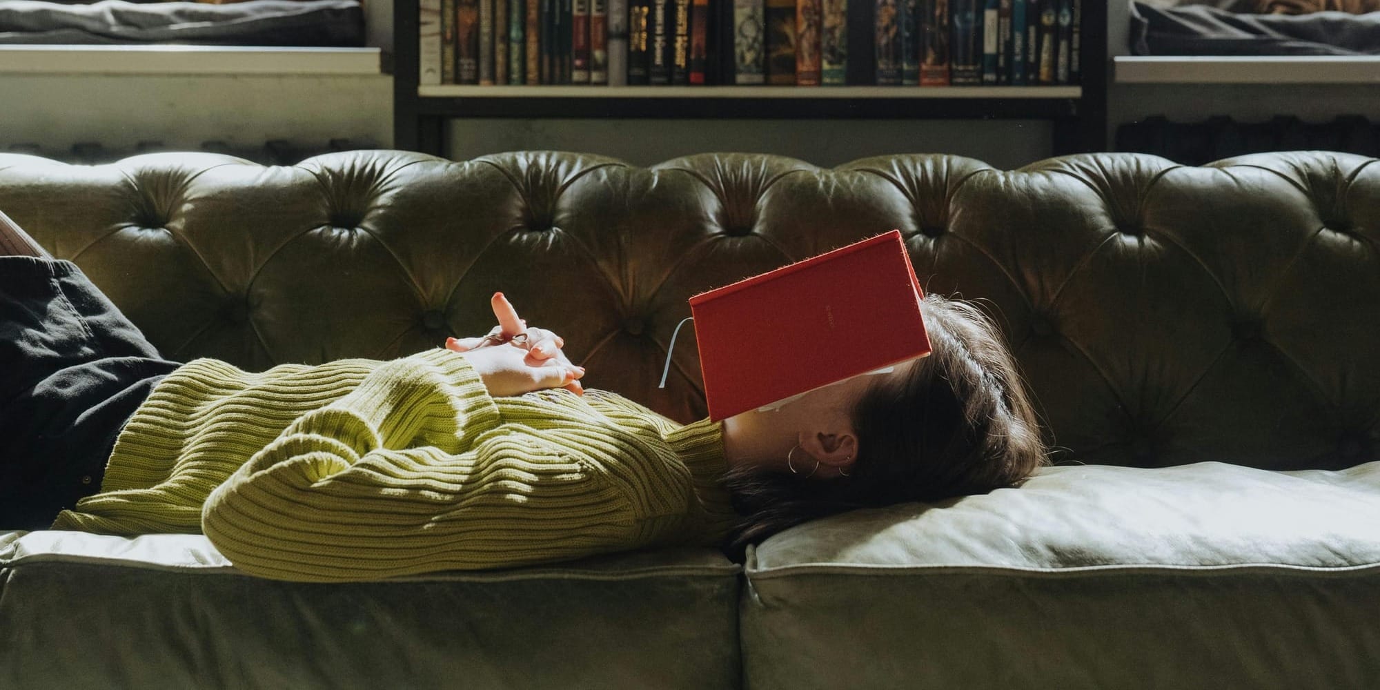Person relaxing on sofa with face covered by book