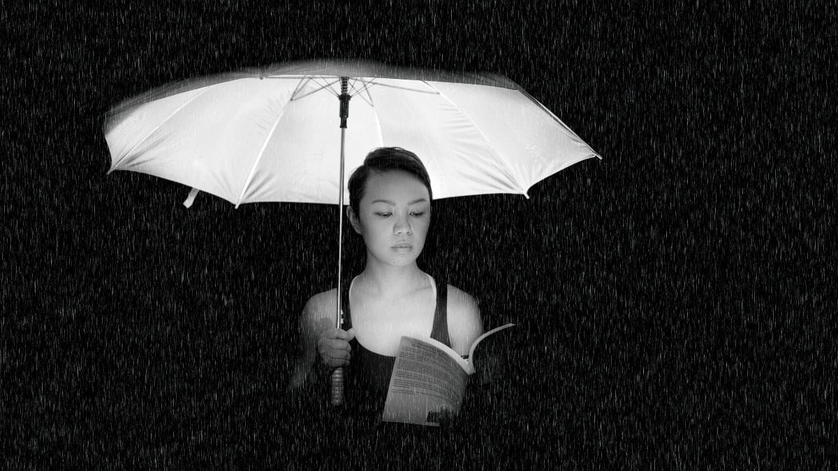 Woman reading a book under an umbrella in the rain