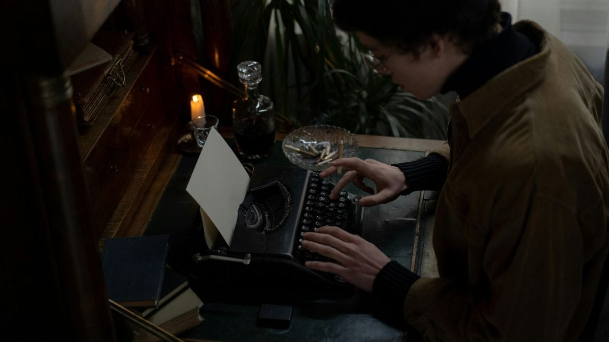 Person writing at vintage typewriter in a dimly lit room