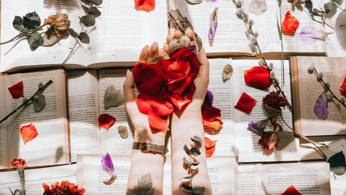 hands with rose petals over books decorated with flowers
