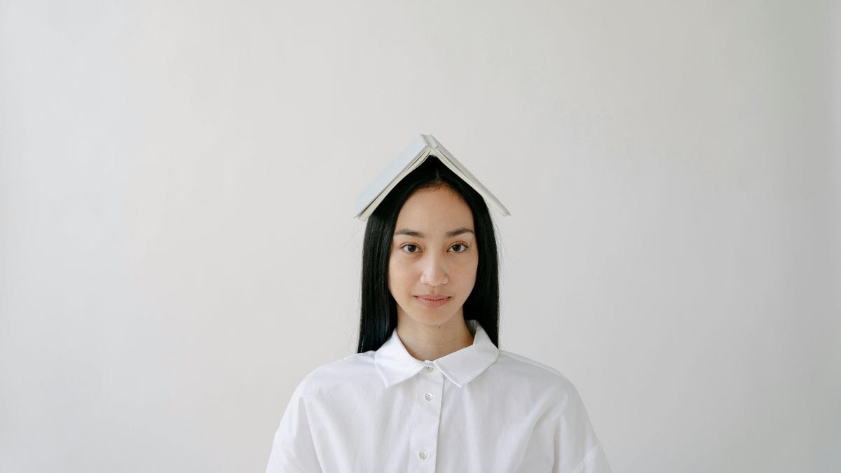 Person with book on head against plain background