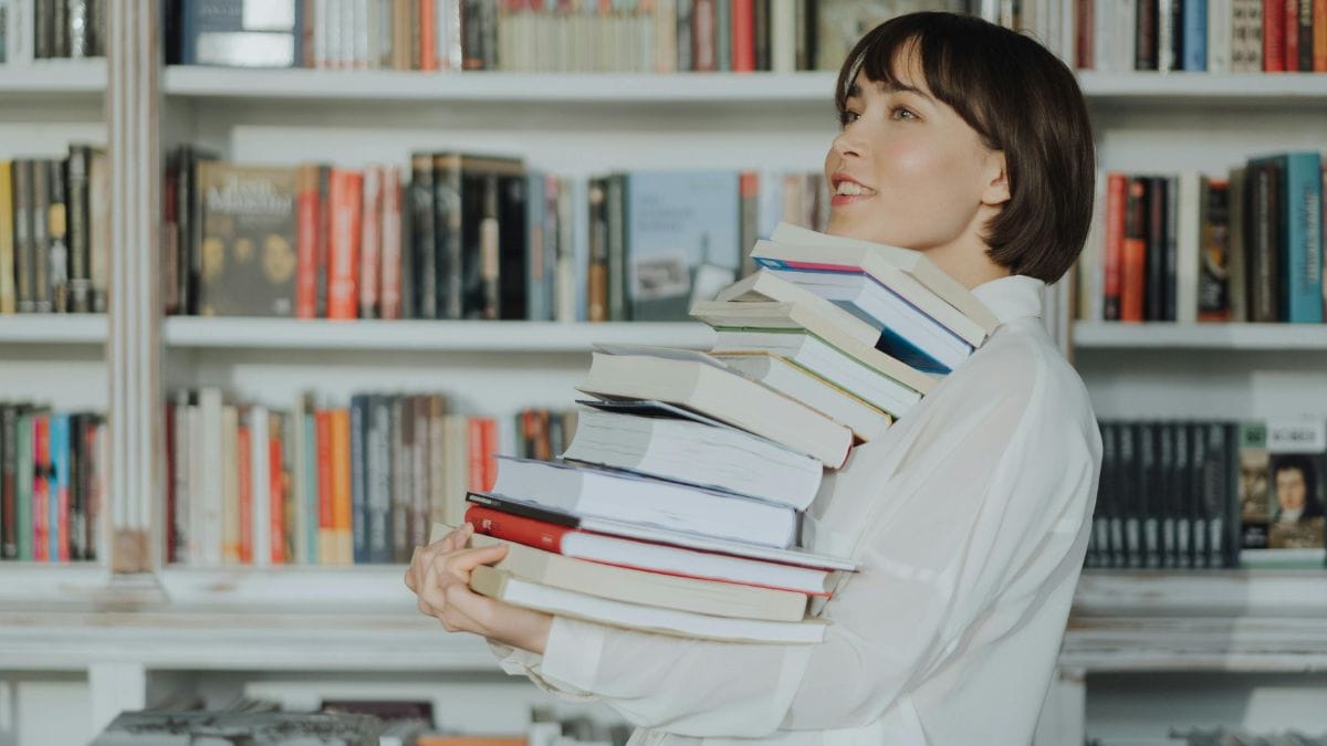 smiling woman holding a stack of books in the library