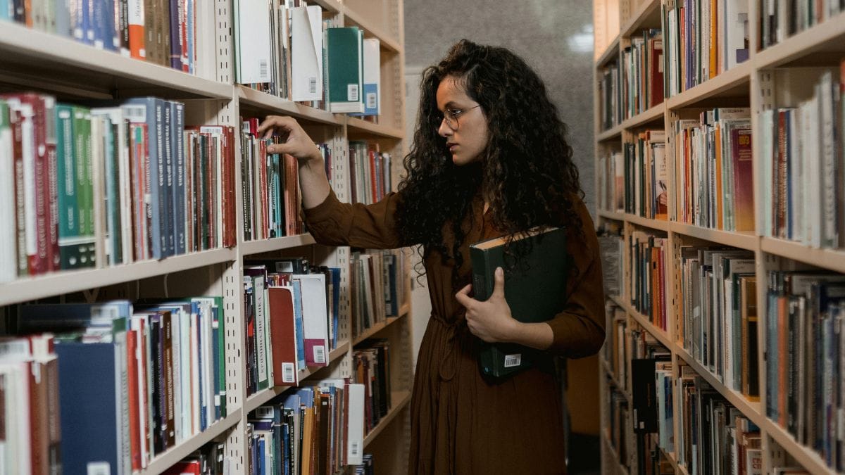 A woman in a library choosing a book from a shelf