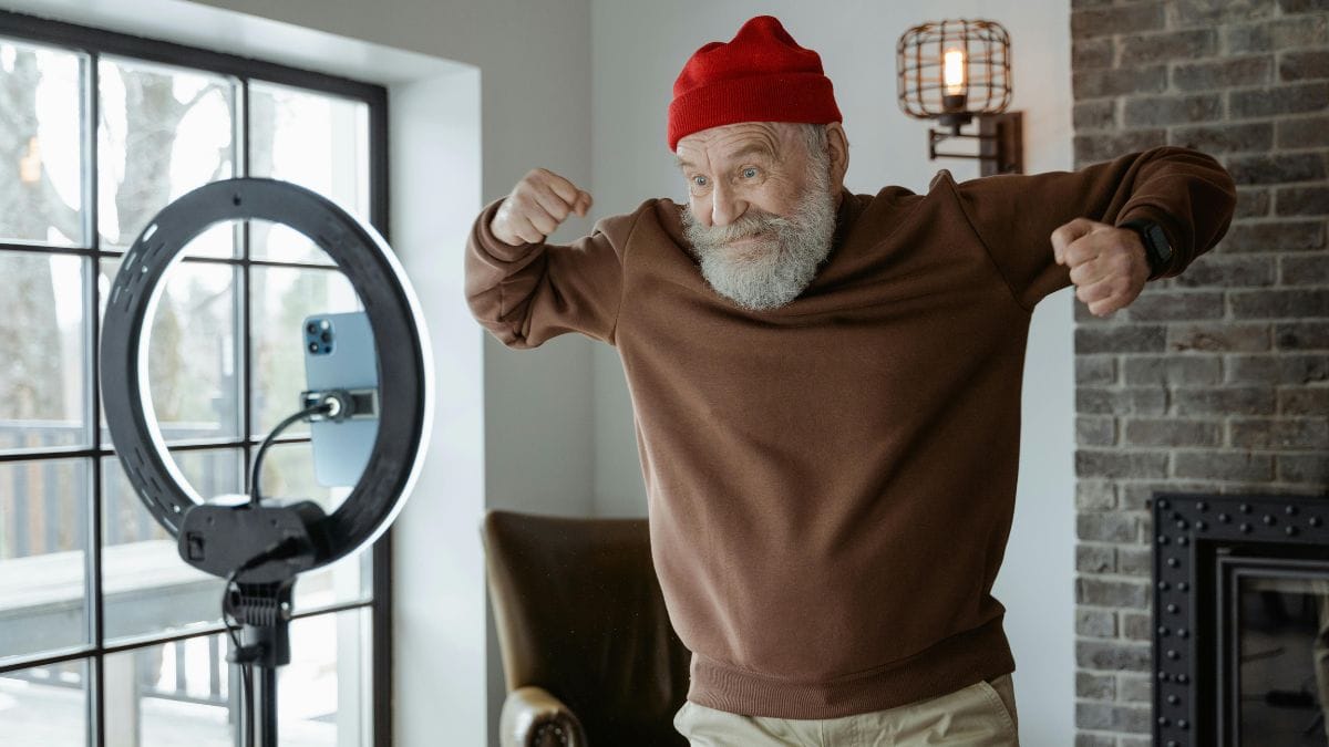 Elderly man recording video at home flexing arms in front of smartphone and ring light.
