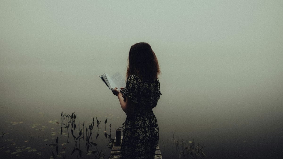 woman reading a book near a lake in the fog