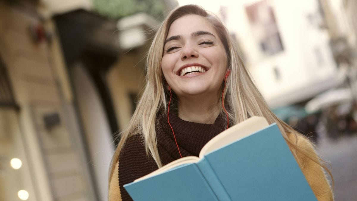 smiling woman with headphones and a book in her hand