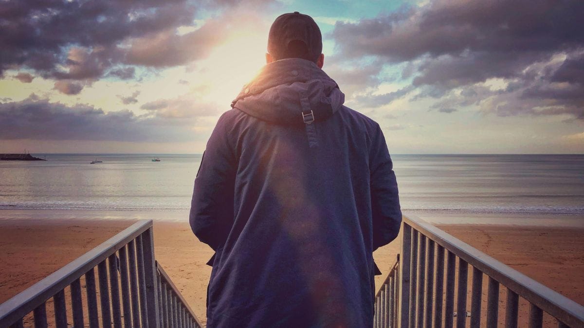 a man walking down to the beach at sunrise
