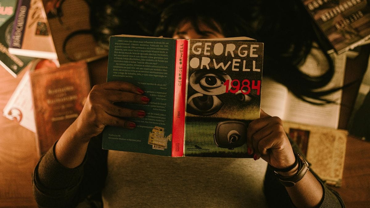 Person reading 1984 by George Orwell surrounded by other books