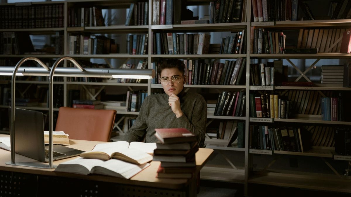a thoughtful man with glasses sitting in a library