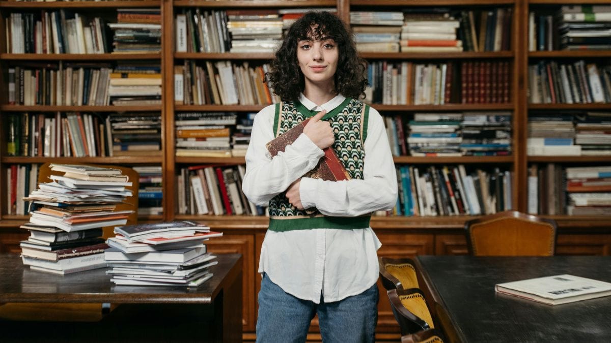 woman holding an old book close to her chest in a library full of books