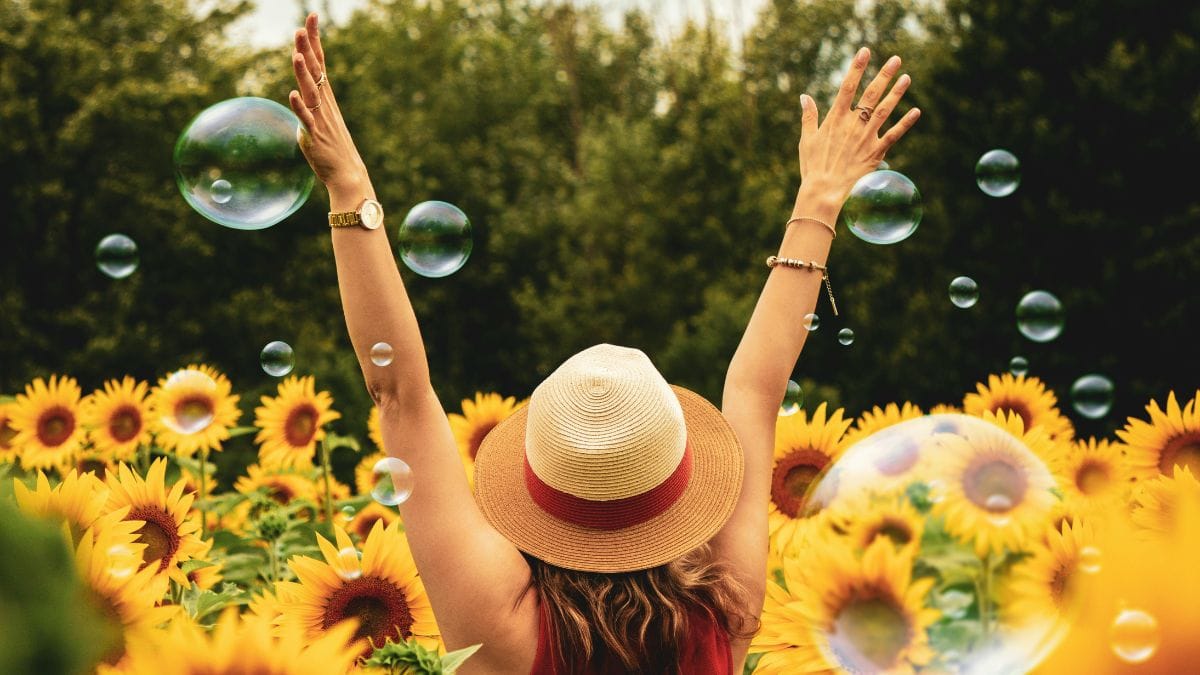 Woman enjoying sunflower field with bubbles in summer outdoors.