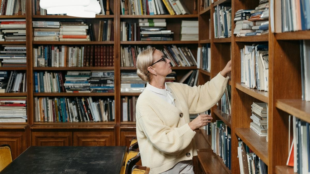 a woman with glasses chooses a book in an old library