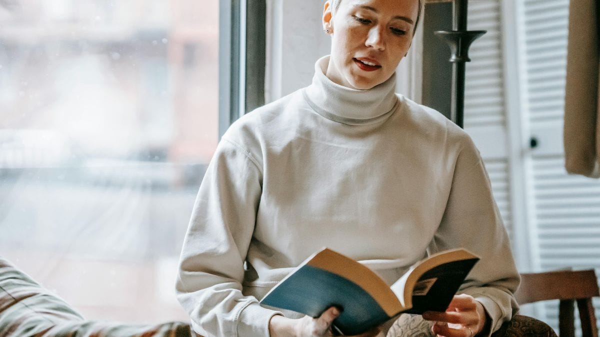slightly smiling woman reading an interesting book near the window