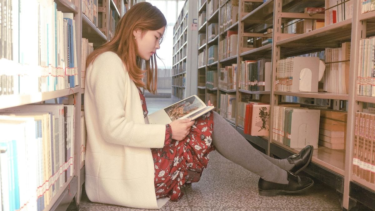 woman sitting on the floor in a library reading a book