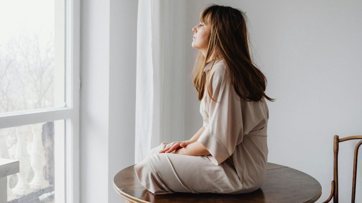 a woman in a cross-legged position looking out the window