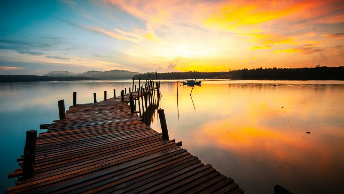 Wooden pier over lake at sunset with colorful sky reflection.