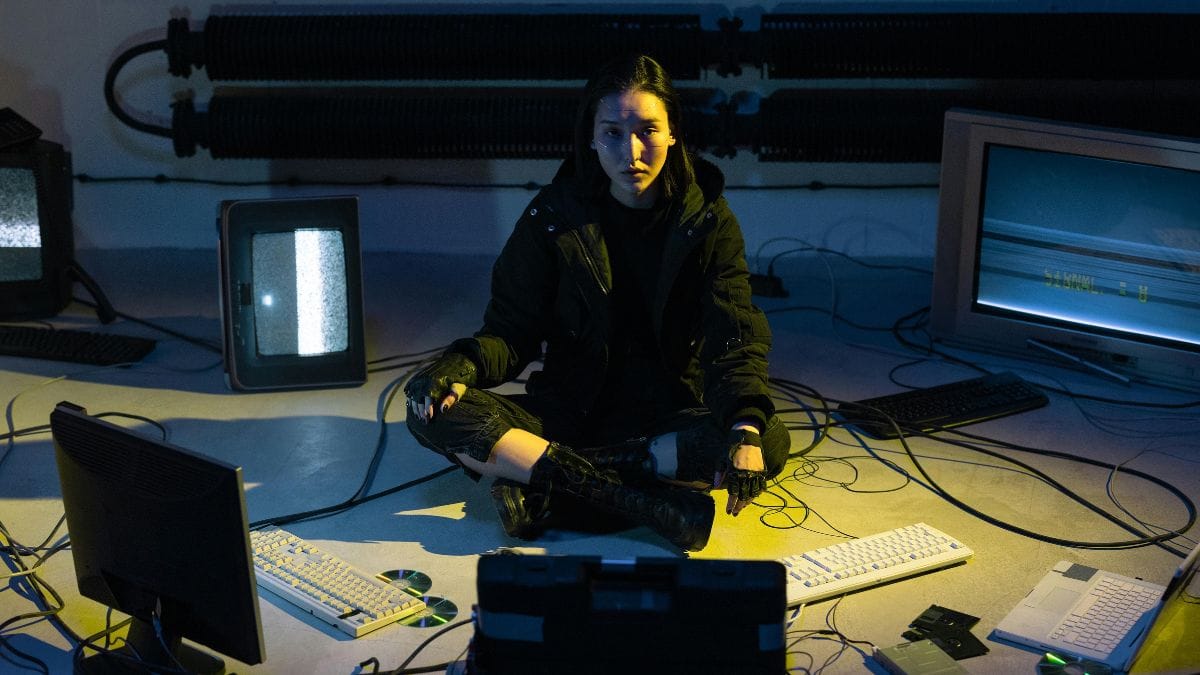 A person sitting cross-legged among old computer monitors and tangled cables
