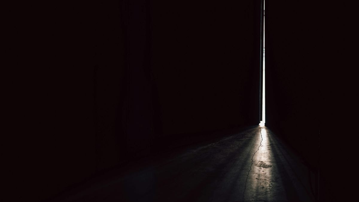 Narrow doorway with a thin line of light in a dark empty space