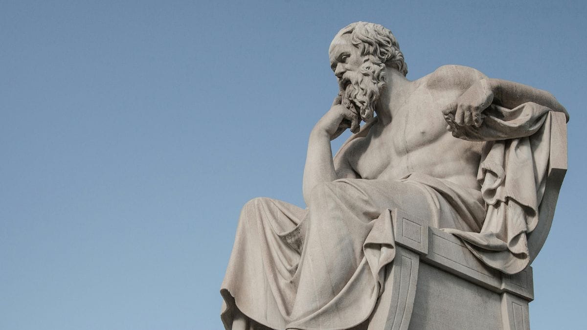 Statue of Socrates seated in thought against a clear blue sky
