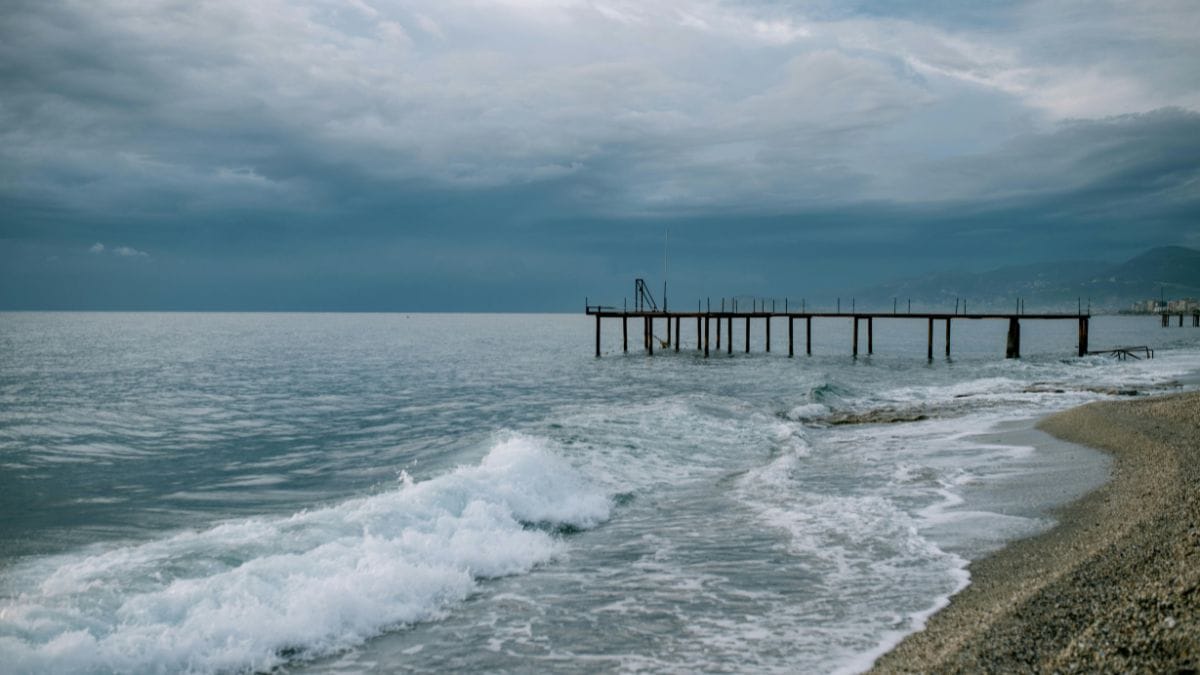 A long pier extending into a calm sea under a heavy, overcast sky.